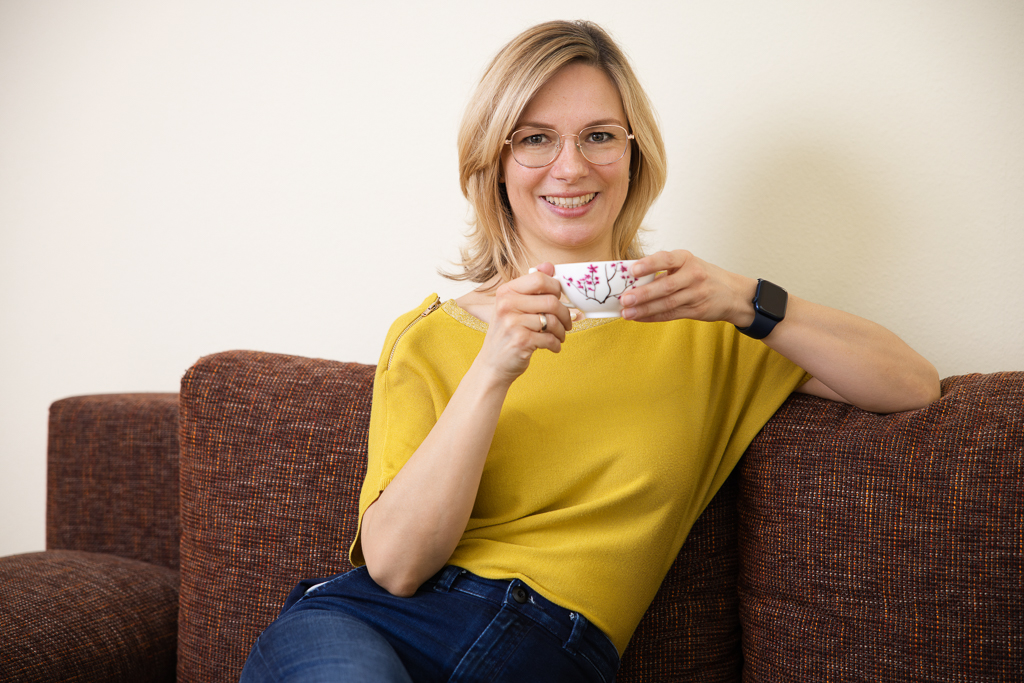 Personal Branding Fotoshooting mit Anne Buckler - systemische Coachin - Koblenz-Gülls - Sitzend mit Kaffeetasse, sie schaut freundlich in die Kamera, gelbes Top und Jeans