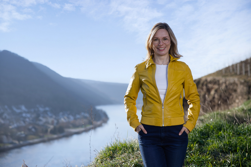 Fotoshooting in der Natur: hier an der Mosel in Koblenz-Güls, Anne steht in den Weinbergen und schaut in die Kamera, gelbe Jacke, Jeans