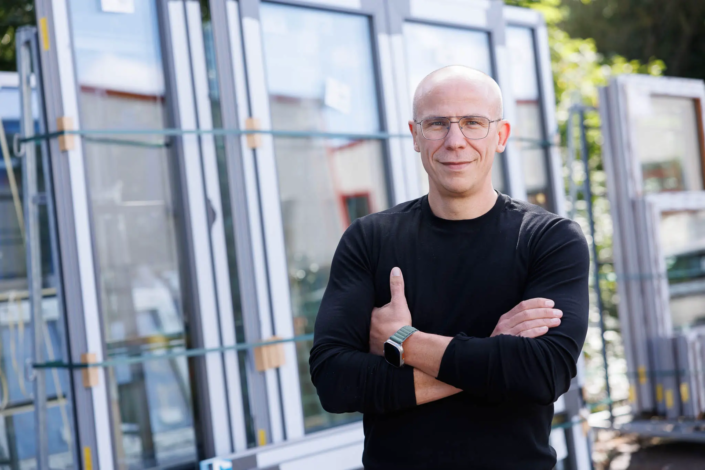 Chef der Firma Hefa Fenster Türen Markisen vor Fenstern stehend.