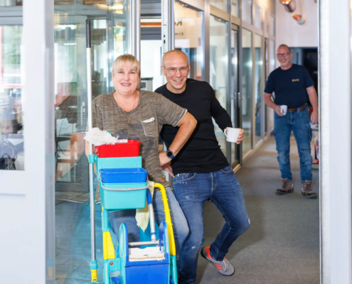 Putzfrau mit Chef der Firma Hefa Fenster Türen Markisen im Büro, die freundlich in die Kamera lächeln.