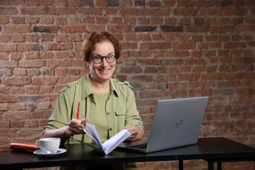 Personal Branding Fotos für die Über-Mich-Seite der Autorin Carla Capellmann, authentisches Portrait der Autorin, das sie mit ihrem Laptop und einem Notizbuch zeigt. Neben ihr steht eine Kaffeetasse.