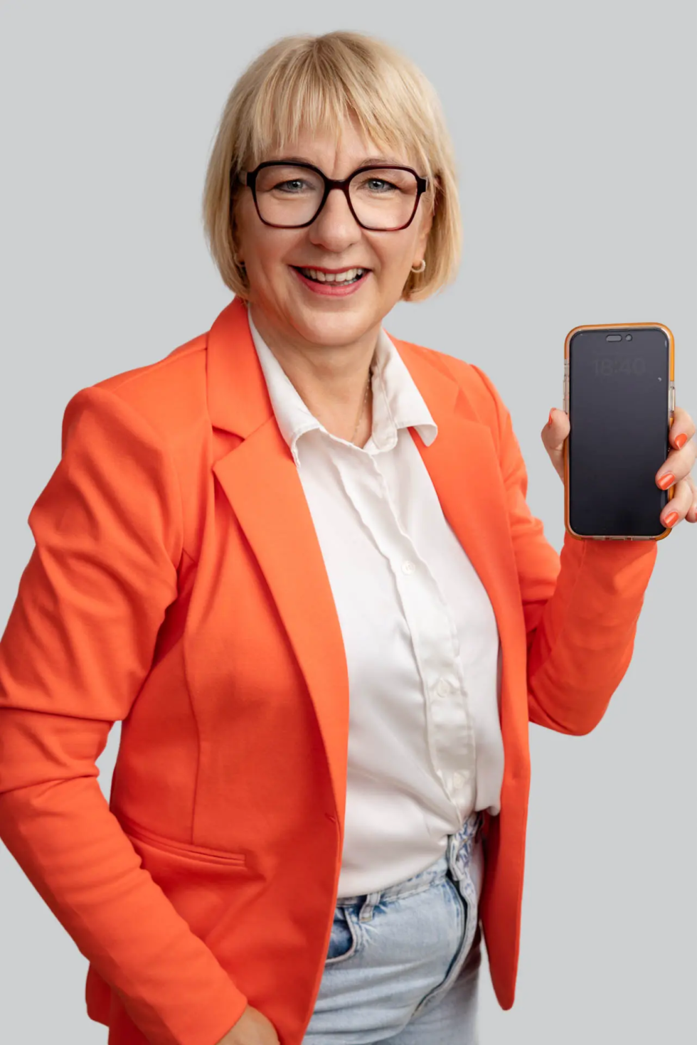 Fotografin Karina Schuh mit orangefarbenem Jacket schaut lächelnd in die Kamera und hält ein Smartphone in der Hand