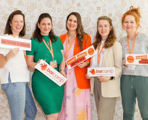 Eine Gruppe von Frauen beim Frauenbarcamp Koblenz 2024 posiert mit Schildern wie „The Future is Female“ und „Frauen stärken jeden Tag“ vor einer Fotowand.