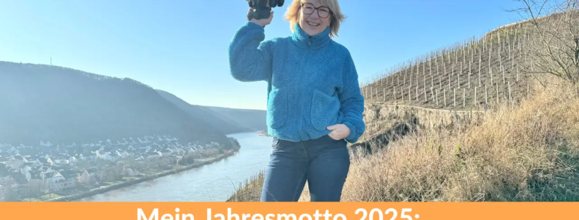 Karina Schuh, Fotografin, in einer entspannten Pose mit Kamera in der Hand, lächelnd vor einer malerischen Landschaft hoch über der Mosel. Text: Mein Jahresmotto 2025 – Leichtigkeit.