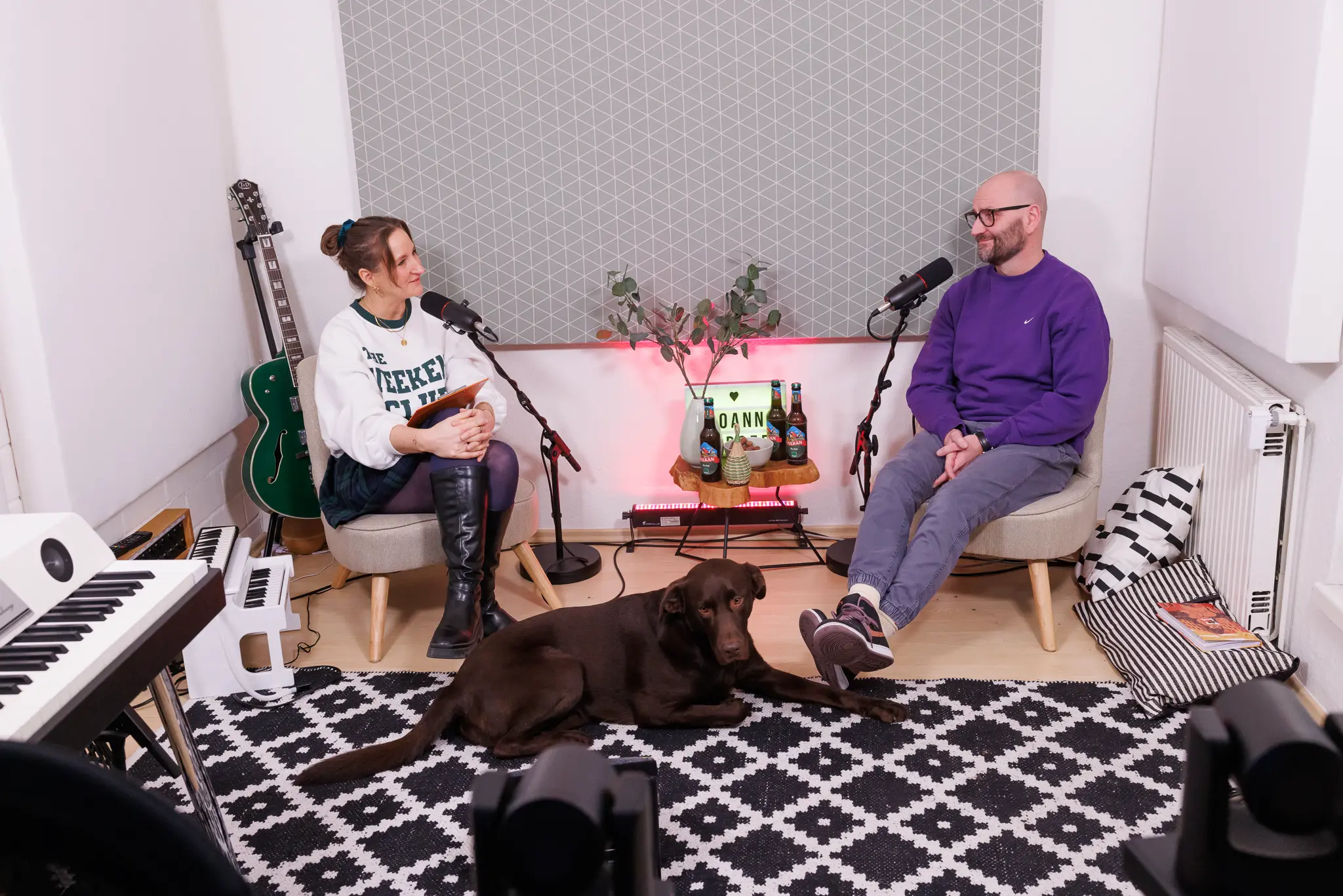 Joanna Gypser und Christian Schmidt unterhalten sich entspannt während des Tiny Studio Talks, während ein brauner Labrador (Kuba) auf dem Teppich liegt.