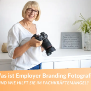 Was ist Employer Branding Fotografie? Fotografin für Unternehmensfotos mit blonden Haaren. Sie schaut in die Kamera und hält selbst eine Kamera in der Hand!