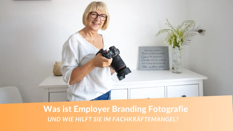 Was ist Employer Branding Fotografie? Fotografin für Unternehmensfotos mit blonden Haaren. Sie schaut in die Kamera und hält selbst eine Kamera in der Hand!