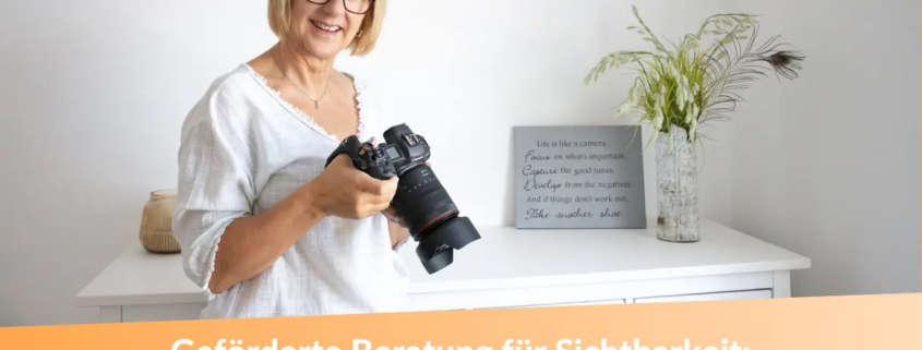 Karina Schuh, Fotografin und Beraterin, lächelt in die Kamera und hält eine professionelle Kamera in der Hand. Im Hintergrund steht ein inspirierendes Zitat. Der Text auf dem Bild lautet: 'Geförderte Beratung für Sichtbarkeit: So stärkst du deine Marke'.