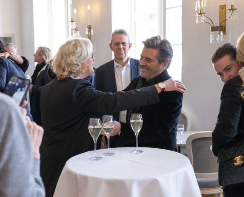 Thomas Anders wird von einer Gästin herzlich bei seinem 60. Geburtstag im Stadttheater Koblenz umarmt. Im Hintergrund sind feiernde Gäste zu sehen.