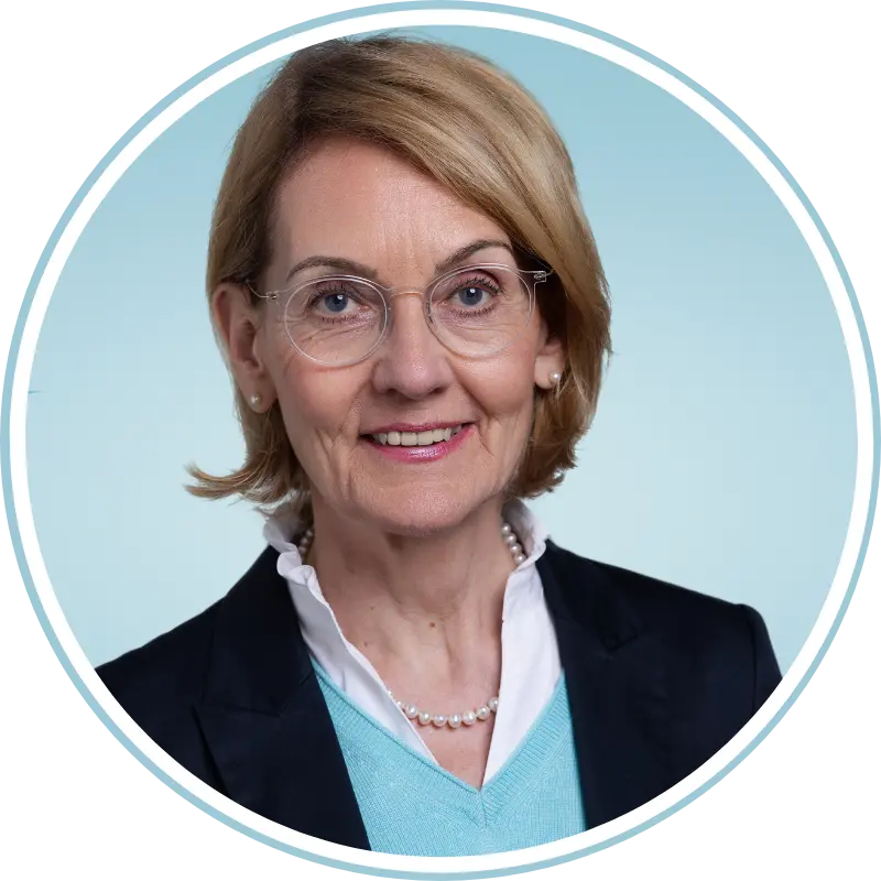 Business-Profilbild einer Frau mit Brille, hellblauem Branding-Hintergrund und klassischem Outfit.