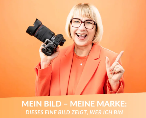 Karina Schuh mit Kamera vor orangefarbenem Hintergrund – Personal Branding Fotografie Markenbild